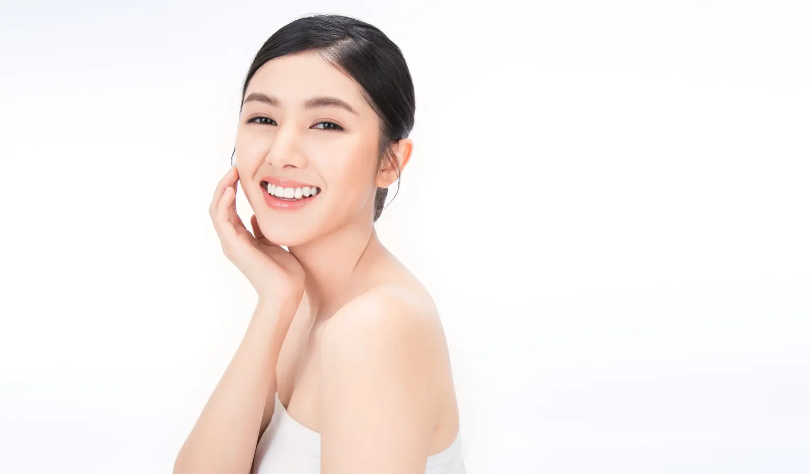Smiling woman with clear skin touching her face against a white background.